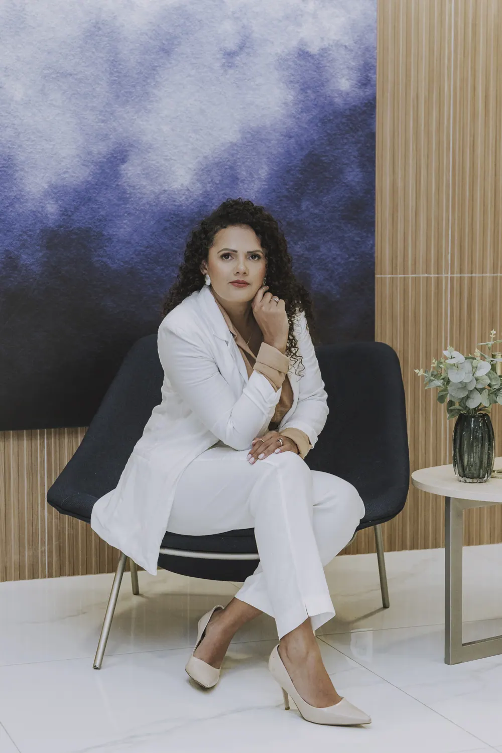 Débora Franca, de terninho branco, sentada numa poltrona azul