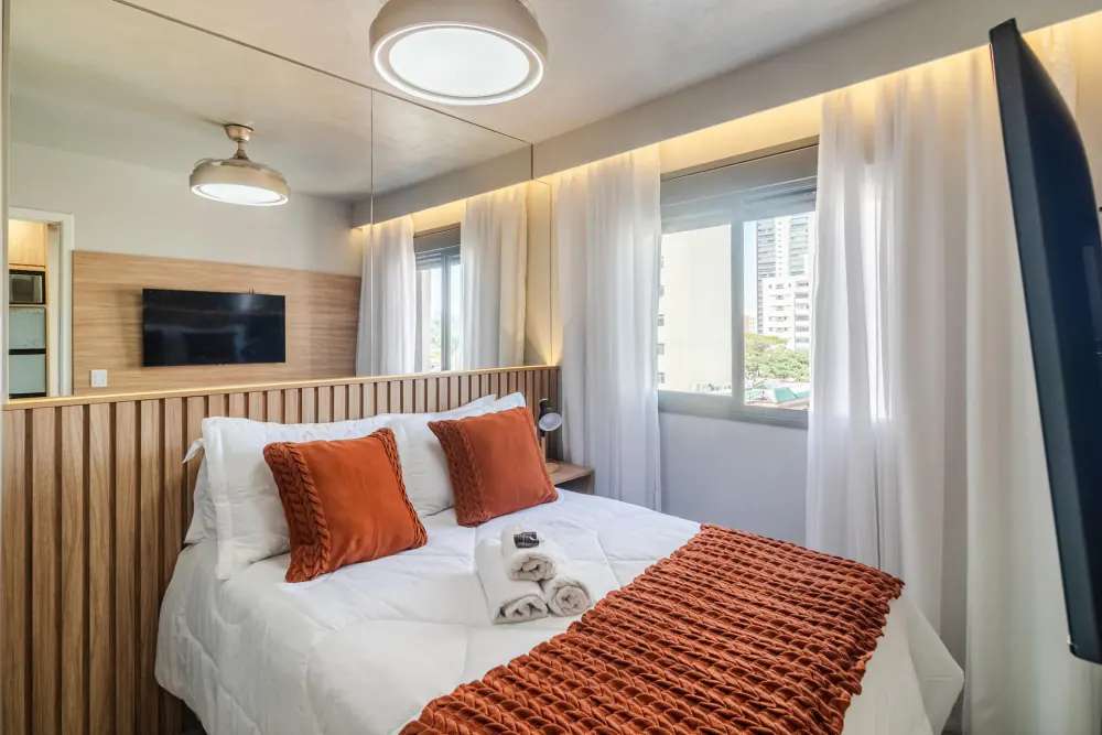 Quarto com cama arrumada e almofadas cor de tijolo, perto da Faria Lima