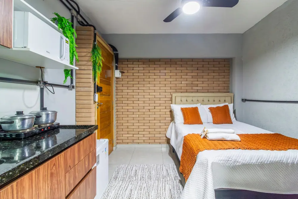 Suíte com parede de tijolinho, cama de casal e cozinha compacta, em Guarulhos