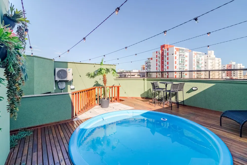 Terraço de um duplex no Guarujá, com piscina privativa, deck de madeira e varal de luzes