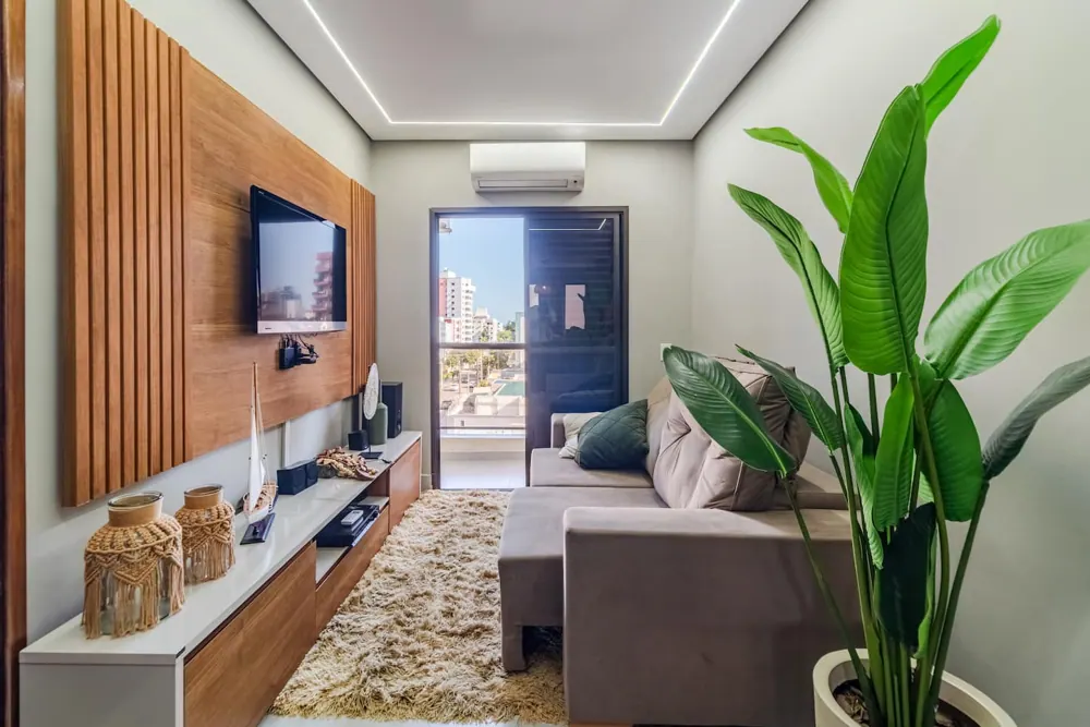 Sala do duplex com sofá retrátil, painel de madeira, TV e porta para a varanda